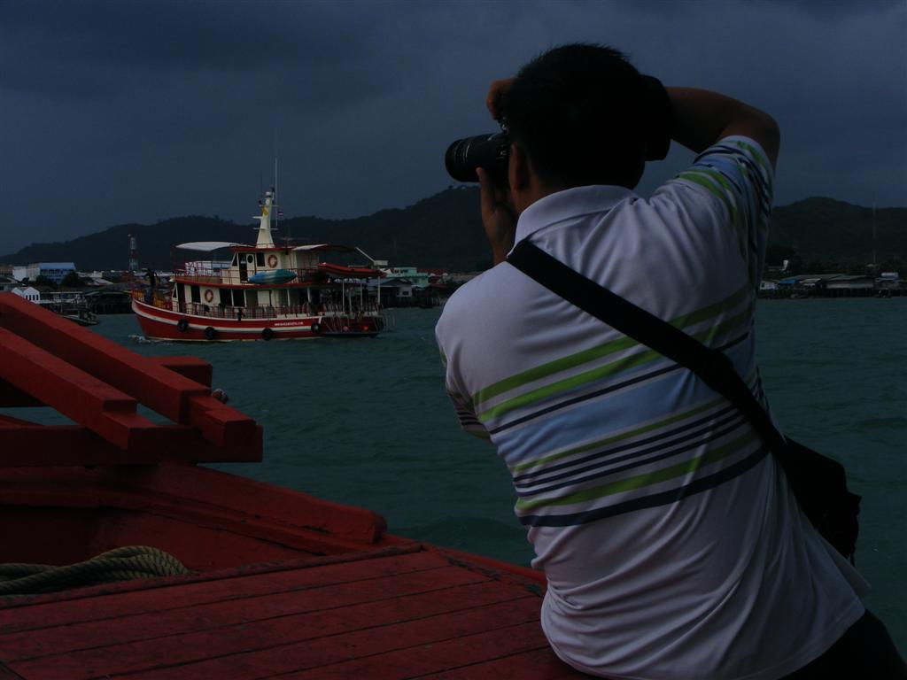           เฮีย ณรงค์ กำลังเก็บภาพของเรือส่งดำน้ำ ที่กำลังเทียบท่าเรืออย่างลำบากเพราะลมที่แรงขึ้นอย่า